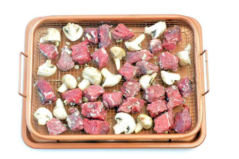 Steak and Mushrooms lined up on an air fryer cookie sheet ready to bake.