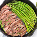 Steak and garlic asparagus cooked in a black cast iron pan.