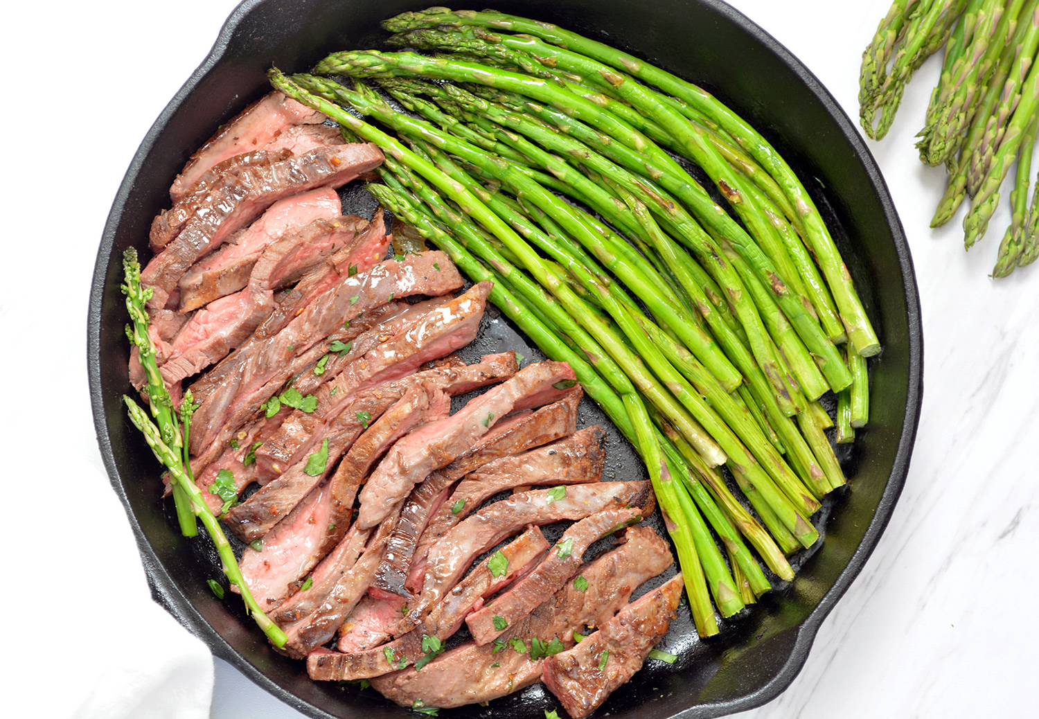 Steak and garlic asparagus cooked in a black cast iron pan.