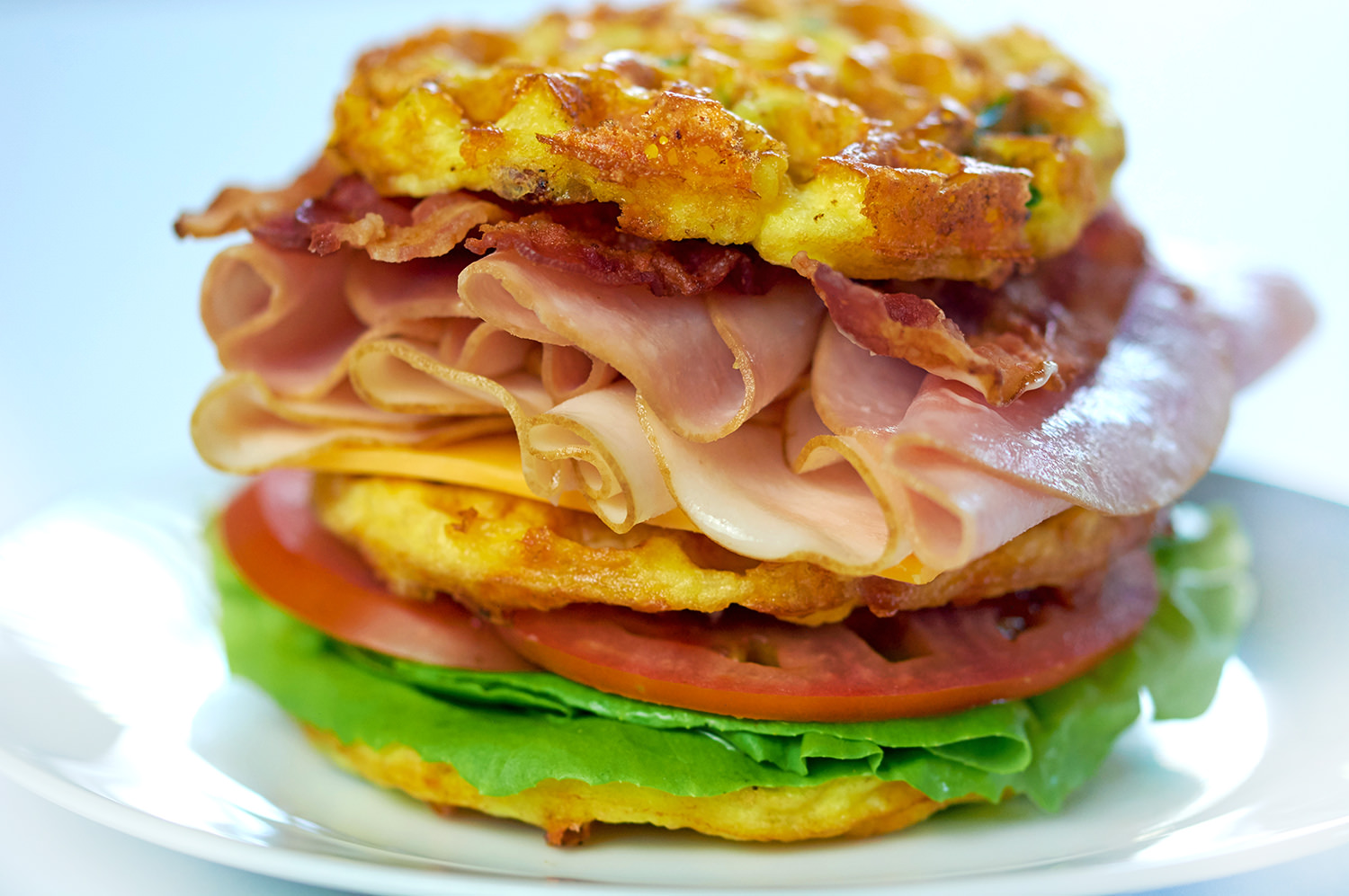 Picture of a Club Sandwich Chaffle on a white plate. Loaded with turkey, ham, cheese and bacon.