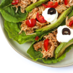 Shredded Chicken in romane lettuce topped with tomatoes, avocado, sour cream, black olives on a white plate