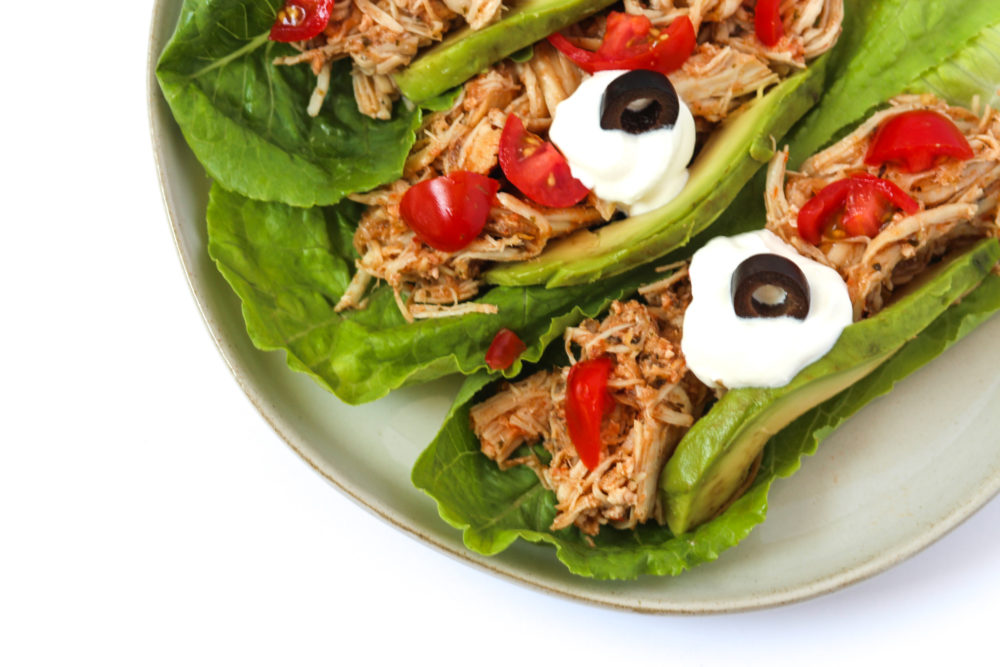 Shredded Chicken in romane lettuce topped with tomatoes, avocado, sour cream, black olives on a white plate