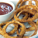 Onion Rings made in the air fryer on a white plate with BBQ sauce dip.