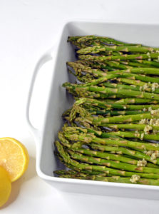 Raw Asparagus with Parmesan and lemon wedge in a white baking dish.