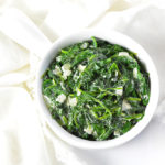 Creamed spinach in a white bowl on a white napkin.