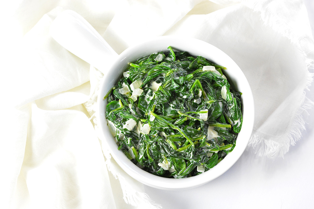 Creamed spinach in a white bowl on a white napkin.