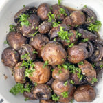 Oven roasted mushrooms in a white bowl topped with parsley.