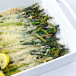 Baked Asparagus with Parmesan and lemon wedge in a white baking dish.