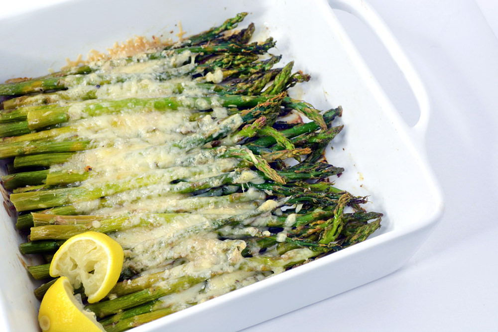 Baked Asparagus with Parmesan and lemon wedge in a white baking dish.