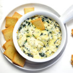 Baked Keto Spinach Dip in a white soup bowl. Rests on a white plate with keto crackers.