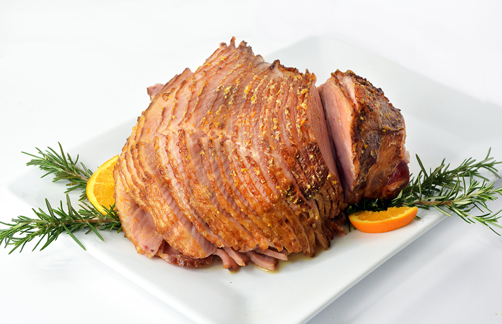 Cooked Crockpot Ham on a white plate surrounded by orange slices.