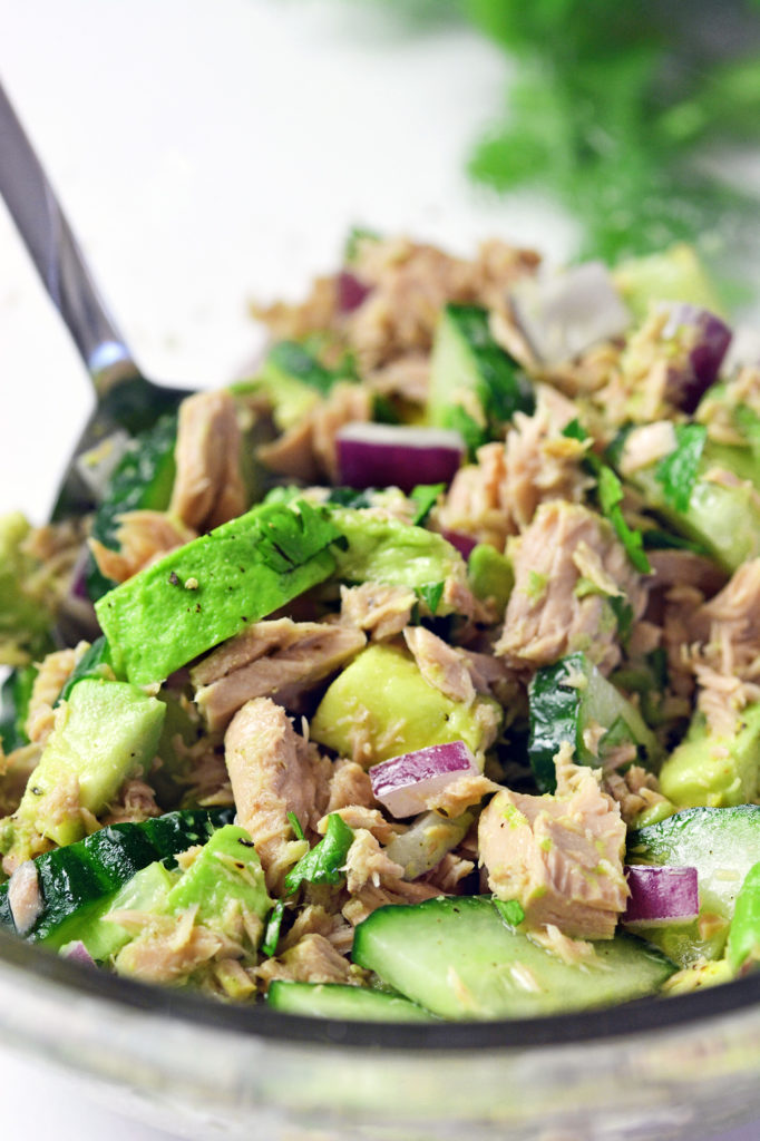 Up close picture of tuna, cucumber, avocado, onions and cilantro being mixed with a silver spoon.