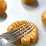 Raw keto peanut butter cookies on a baking sheet being smashed by a silver fork.