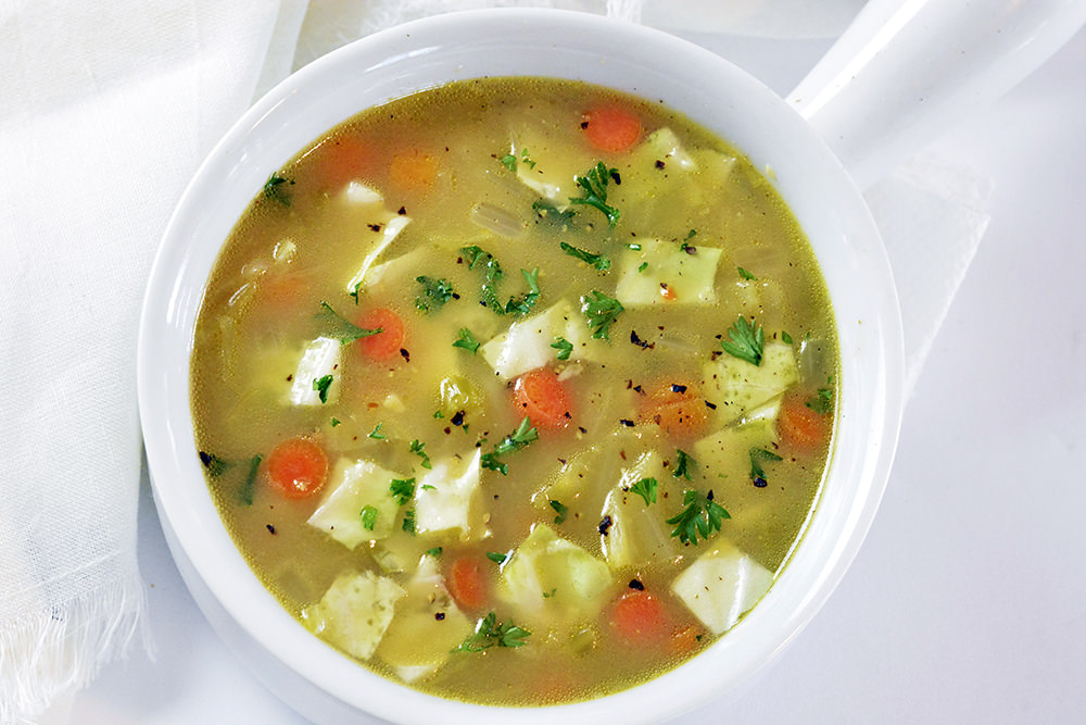 How To Make Cabbage Soup Tutorial. Cabbage Soup in a white soup bowl surrounded by a white napkin.