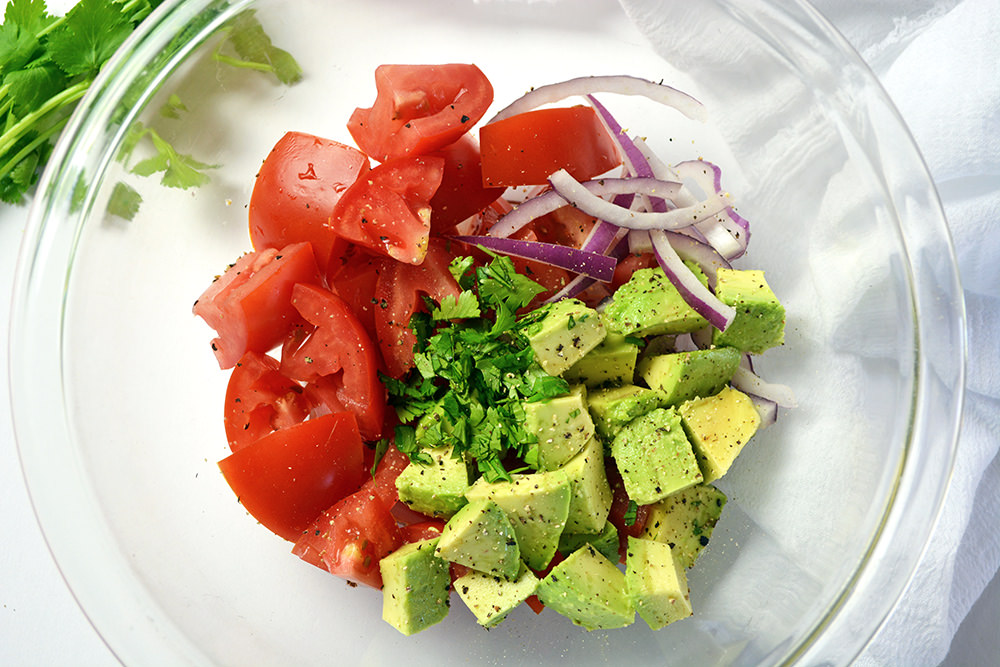 Picture of diced tomatoes, diced avocado, diced onions and cilantro in a clear mixing bowl.