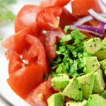 Up close picture of tomatoes, avocado, onions and cilantro un-mixed in a clear bowl.