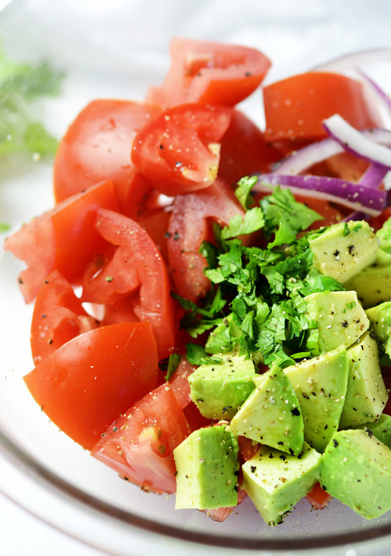 Up close picture of tomatoes, avocado, onions and cilantro un-mixed in a clear bowl.