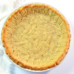 Baked low carb pie crust with almond flour in a clear glass pie pan on top of a white table..