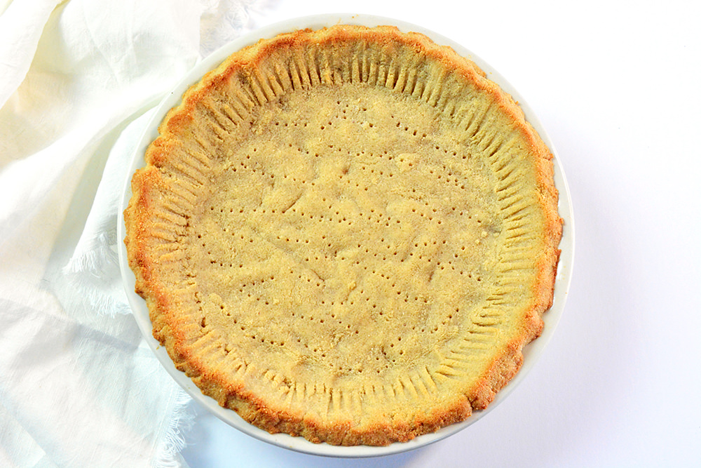 Baked low carb pie crust with almond flour in a clear glass pie pan on top of a white table..