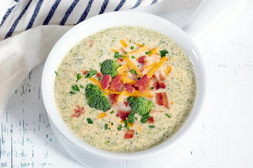 Keto Broccoli Cheese Soup in a white soup bowl topped with crumbled bacon and cheese.