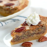 slice of pecan pie on a white plate topped with a dollop of whipped cream.