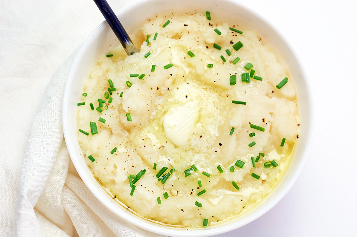 White bowl filled with Keto Mashed Cauliflower topped with chives and melted butter.