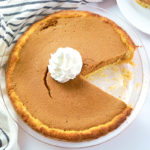 Keto pumpkin pie topped with whipped cream. Once slice is cut out and placed to the side next to a blue and cream napkin.