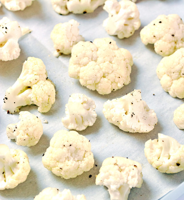 Picture of cauliflower florets covered in salt and pepper on a parchment lined cookie sheet.