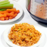 A bowl full of shredded buffalo chicken next to an Instant Pot and plate full of carrots and celery.