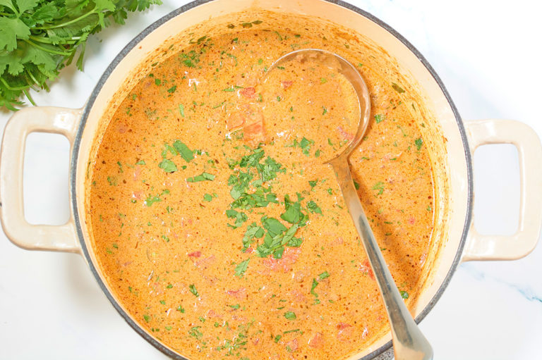 A white pot filled with keto taco soup topped with chopped cilantro. A soup ladle is inside the pot and a bunch of cilantro is next to the pot.