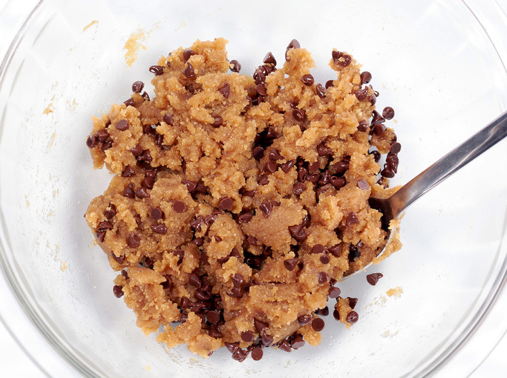 cookie dough batter mixed together in a glass bowl with a stainless steel spoon