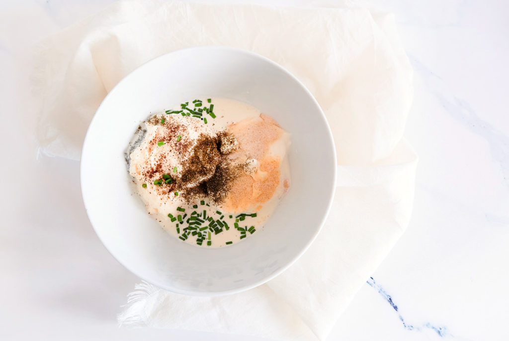 White bowl with keto ranch dressing ingredients before being mixed. The bowl is placed on a white napkin.