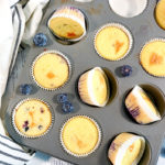 Overhead shot of cooked Keto Blueberry Muffins in a muffin tin. A side of blueberries is next to it.