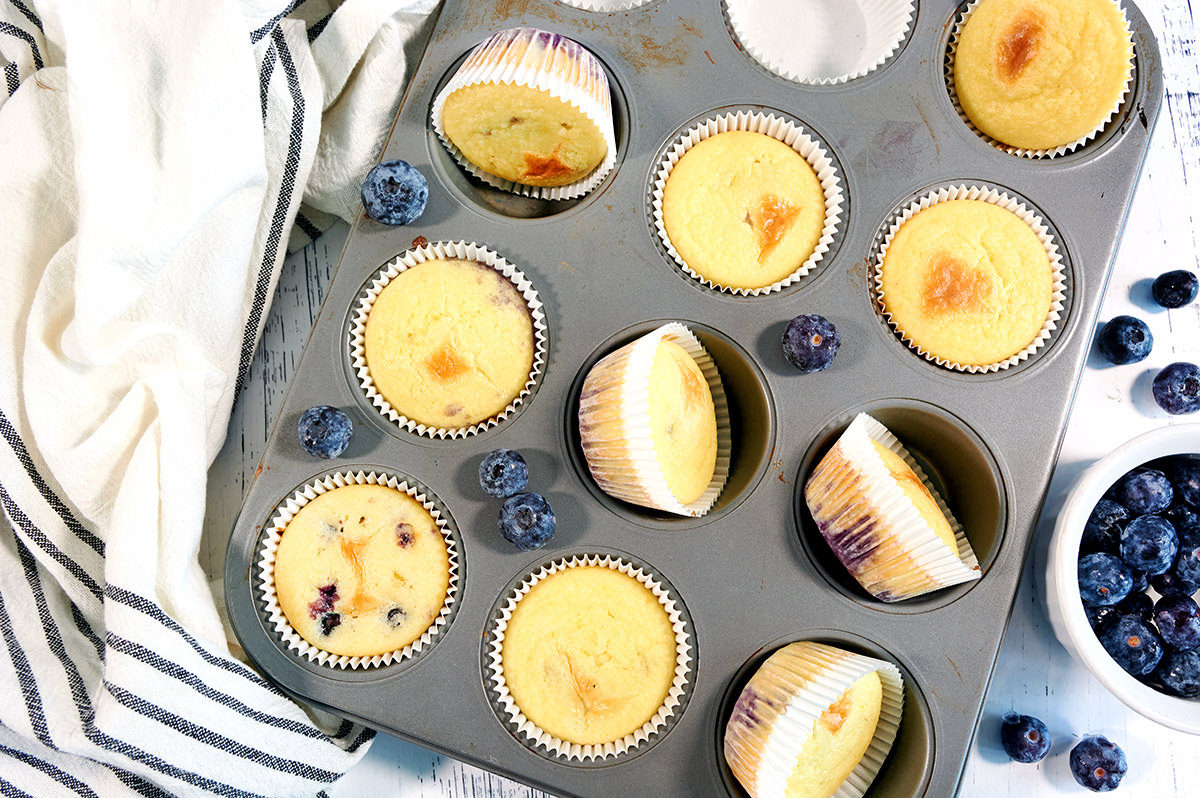 Overhead shot of cooked Keto Blueberry Muffins in a muffin tin. A side of blueberries is next to it.